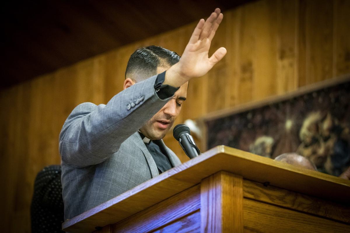 Pastor Gonzalez raising his hand in blessing at the lectern